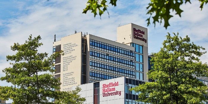 A photo of the the Sheffield Hallam University building with logos and signage, taking through the trees.