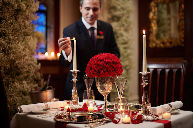 An image of a male waiter working at Red Carnation Hotel (CTH Gold Employer), lighting a candle at a luxurious table/dining area.